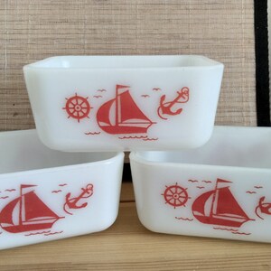 May include: Three white ceramic rectangular baking dishes with red nautical designs. Each dish features a sailboat, anchor, and steering wheel.