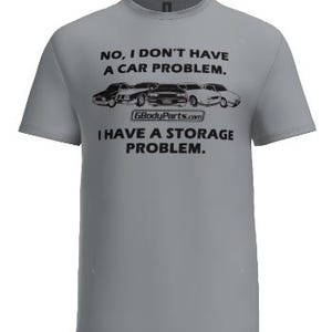 Puede incluir: Una camiseta gris con el texto "NO, I DON'T HAVE A CAR PROBLEM. I HAVE A STORAGE PROBLEM." y un gráfico de coches clásicos. El sitio web GBodyParts.com también está impreso en la camiseta.