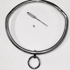 May include: A silver metal choker necklace with a round ring attached. The necklace is made of a thick, sturdy metal and has a simple, elegant design.