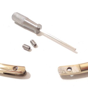 K&ouml;nnte beinhalten: Eine goldfarbene, offene Halskette mit einem kleinen Schraubendreher und zwei kleinen Schrauben. Die Halskette besteht aus gl&auml;nzendem Metall und hat an einem Ende einen Verschluss. Der Schraubendreher ist silberfarben und hat einen strukturierten Griff.