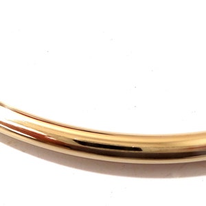 K&ouml;nnte beinhalten: Ein Abschnitt eines goldfarbenen, gebogenen Metallobjekts, m&ouml;glicherweise ein Armband oder eine Halskette. Die Oberfl&auml;che reflektiert Licht und erzeugt Glanzlichter und Schatten. Der Hintergrund ist schlicht wei&szlig;.