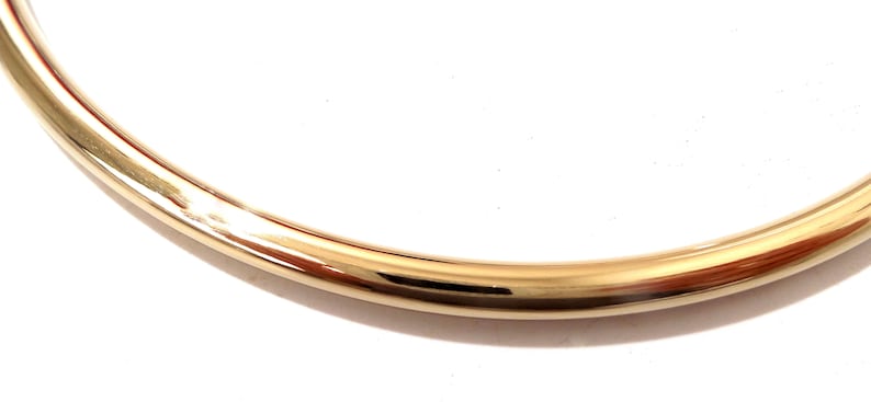 K&ouml;nnte beinhalten: Ein Abschnitt eines goldfarbenen, gebogenen Metallobjekts, m&ouml;glicherweise ein Armband oder eine Halskette. Die Oberfl&auml;che reflektiert Licht und erzeugt Glanzlichter und Schatten. Der Hintergrund ist schlicht wei&szlig;.