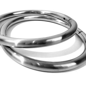 May include: Two silver metal rings, one slightly larger than the other, are stacked on top of each other. The rings are smooth and have a polished finish.