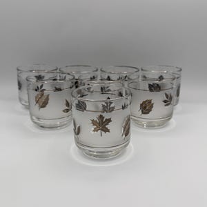 May include: A set of nine clear glass tumblers with a frosted finish. Each tumbler features a silver and gold leaf design. The glasses are arranged in a group, showcasing their decorative details and vintage style.