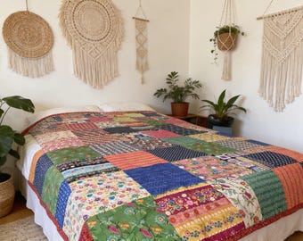 May include: A patchwork quilt with a variety of colorful fabric squares covers a bed. The quilt features floral, geometric, and solid patterns in shades of green, blue, pink, and orange. The bed is against a white wall with macrame wall hangings.