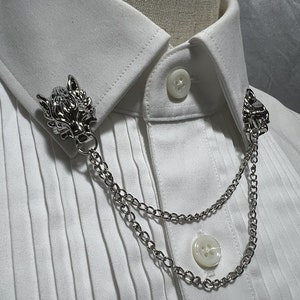 May include: A silver wolf head collar clip with a silver chain. The clip is attached to a white collared shirt.