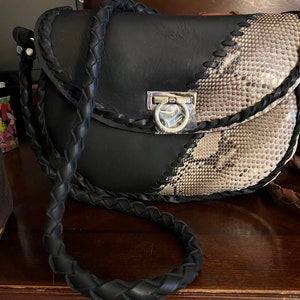 Pode incluir: Uma bolsa de ombro de couro preto e pele de cobra com uma alça trançada e um fecho prateado.