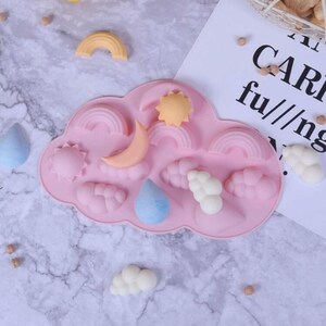 May include: Pink silicone mold shaped like a cloud with various shapes for making soap or candles. The shapes include a sun, moon, rainbow, and raindrops.