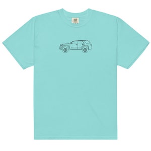 以下が含まれることがあります： 薄い青色のTシャツで、前面に黒い線で描かれた車の絵が描かれています。