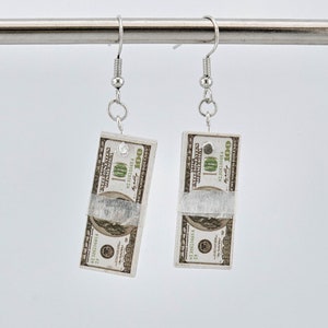 May include: A pair of silver earrings with a folded £100 note charm on each earring.