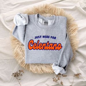 May include: Gray sweatshirt with the text "Just here for Celentano" in orange and blue lettering.
