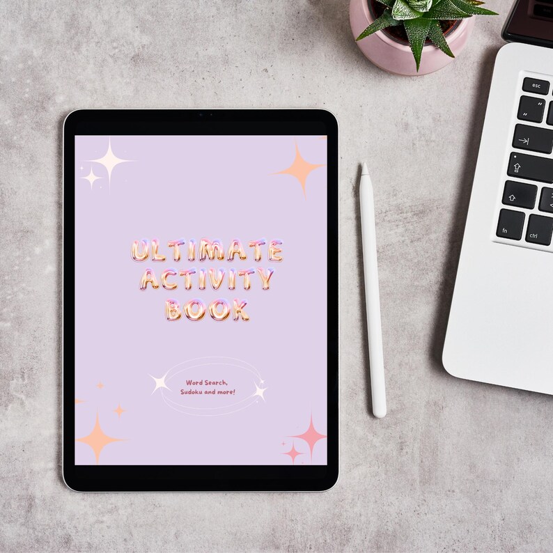 May include: A purple tablet screen displaying a digital activity book cover with the text "ULTIMATE ACTIVITY BOOK" in a pink and orange font. The cover also includes the text "Word Search, Sudoku and more!" in a smaller font. The tablet is on a gray surface with a white stylus and a laptop in the background.