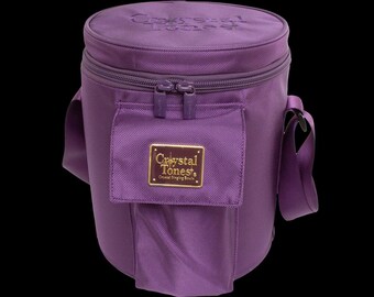 May include: A cylindrical, purple carrying bag with a zippered top and a front pocket. The bag has a shoulder strap and a gold-colored label that reads "Crystal Tones". The top of the bag has the words "Crystal Tones" embroidered on it.