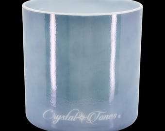 May include: A cylindrical, light blue crystal singing bowl with a glossy finish. The bowl has a white rim and the words "Crystal Tones" are printed in a cursive font on the side. The background is black.