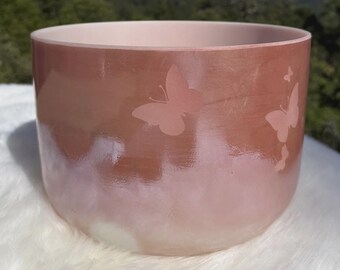 May include: A pink and peach-colored bowl with a glossy finish. The bowl features etched butterfly designs and a gradient effect, transitioning from a darker peach at the top to a lighter pink at the base. The bowl is likely used for decorative purposes.