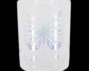 May include: A white glass candle holder with a large butterfly design in iridescent colors. The butterfly is centered on the front of the holder, with floral accents at the bottom. The candle holder is cylindrical.