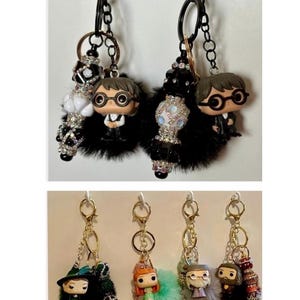 May include: Keychains featuring character figurines with black fur accents and decorative beads. The keychains have gold and black hardware. The figurines include characters with glasses, hats, and colorful outfits. The keychains are attached to a black metal ring.