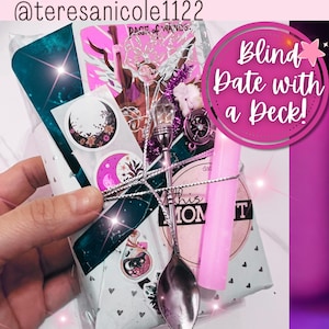 Op de afbeelding: Een verpakt cadeaupakket met een zilveren lepel, een roze kaars en stickers. Het pakket is vastgebonden met zilveren touw en bevat een tarotkaart met de tekst "PAGE of WANDS". Een roze cirkel leest "Blind Date with a Deck!"