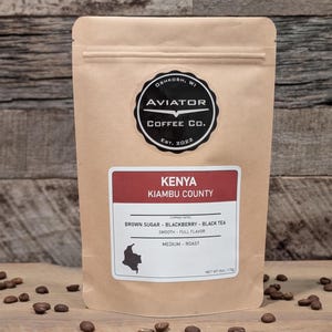 May include: A brown paper bag with a label that says "Kenya Kiambu County" and "Aviator Coffee Co. Est. 2022". The label also lists the coffee's tasting notes: "Brown Sugar - Blackberry - Black Tea", "Smooth - Full Flavor", and "Medium Roast".