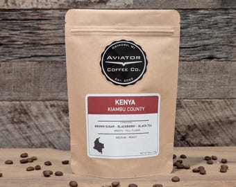 Puede incluir: Una bolsa de papel marrón con una etiqueta que dice "Kenya Kiambu County" y "Aviator Coffee Co. Est. 2022". La etiqueta también enumera las notas de sabor del café: "Brown Sugar - Blackberry - Black Tea", "Smooth - Full Flavor" y "Medium Roast".