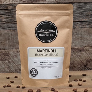 May include: A brown paper bag of Martinoli Espresso Blend coffee from Aviator Coffee Co. The bag has a black and white circular logo and a label with tasting notes. The bag contains 8 oz of coffee.