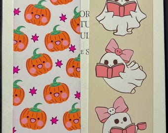 May include: Two decorative bookmarks. One features a pattern of orange pumpkins with green stems and pink stars. The other has three white ghost illustrations with pink bows and books. One ghost holds a cup. The text "OR TUI ES" is visible.