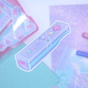 May include: A light blue and purple video game controller sticker with pink and white buttons. The sticker is on a sparkly background.