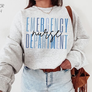 May include: A light gray sweatshirt with the words "EMERGENCY NURSE DEPARTMENT" in blue and black lettering. The sweatshirt is a light ash color. The text "COLOR ASH" is in the upper left corner.