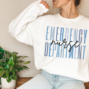 May include: White sweatshirt with the words "EMERGENCY NURSE DEPARTMENT" printed in blue and black. The text is stacked vertically, with "nurse" in a handwritten font. The sweatshirt is a crew neck style.