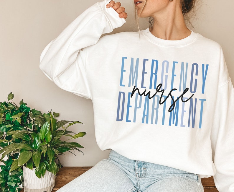 May include: White sweatshirt with the words "EMERGENCY NURSE DEPARTMENT" printed in blue and black. The text is stacked vertically, with "nurse" in a handwritten font. The sweatshirt is a crew neck style.