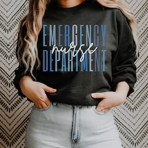 May include: Black sweatshirt with the words "EMERGENCY nurse DEPARTMENT" in blue and white lettering. The word "nurse" is in a cursive font. The sweatshirt is worn with light blue jeans.