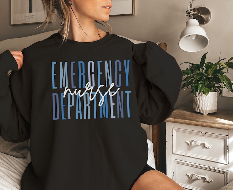 May include: Black sweatshirt with the words "EMERGENCY nurse DEPARTMENT" in blue and white lettering. The word "nurse" is in a cursive font. The sweatshirt is a crew neck style.