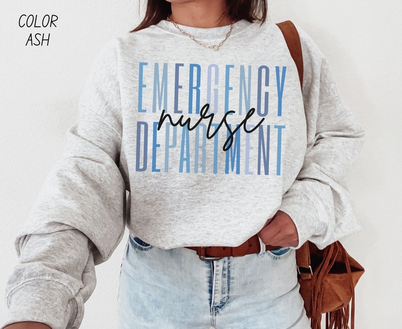 May include: A light gray sweatshirt with the words "EMERGENCY NURSE DEPARTMENT" in blue and black lettering. The sweatshirt is a light ash color. The text "COLOR ASH" is in the upper left corner.
