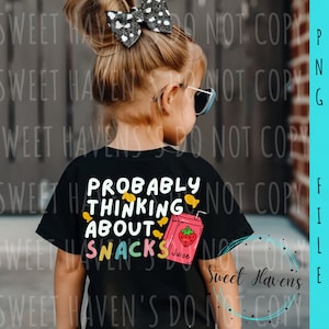 Pode incluir: Uma criança vestindo uma camiseta preta com o texto "Probably Thinking About Snacks" e uma ilustração de desenho animado de uma caixa de suco com um morango.