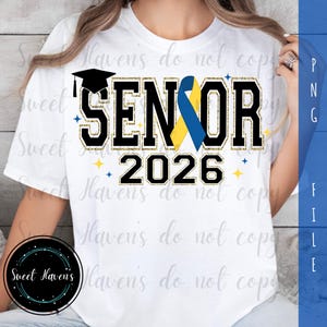May include: White t-shirt with the word "SENIOR" in black block letters with gold glitter trim and a blue and yellow ribbon. The year "2026" is below the word "SENIOR". A graduation cap is above the word "SENIOR".