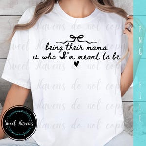 Könnte beinhalten: Weißes T-Shirt mit dem schwarzen Schriftzug "being their mama is who I'm meant to be", verziert mit einer Schleife und einem Herz. Ein lässiges Oberteil für Mütter.