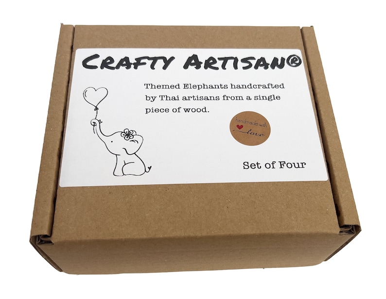 May include: A brown cardboard box with a white label that says "CRAFTY ARTISANO&reg;" and "Themed Elephants handcrafted by Thai artisans from a single piece of wood. handmade with love Set of Four". The label has a black and white illustration of an elephant holding a heart-shaped balloon.