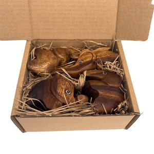 May include: Four wooden elephant figurines in a brown cardboard box with shredded paper packing. The elephants are all facing different directions and have a natural wood finish.