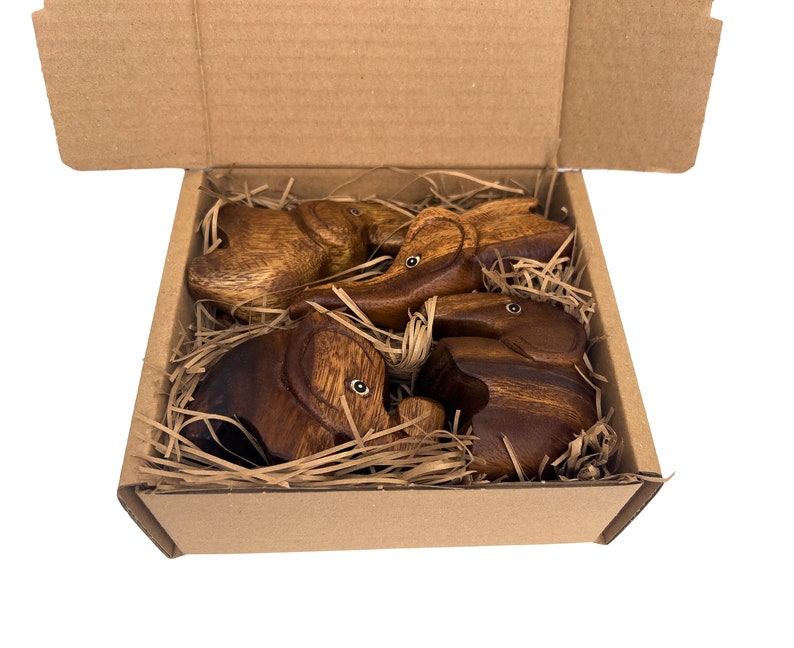 May include: Four wooden elephant figurines in a brown cardboard box with shredded paper packing. The elephants are all facing different directions and have a natural wood finish.