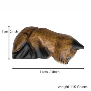 May include: Hand-carved wooden cat figurine in a crouching position. The cat is brown with black markings and blue eyes. It measures 4 inches long and 2 inches tall. weight 110 Grams