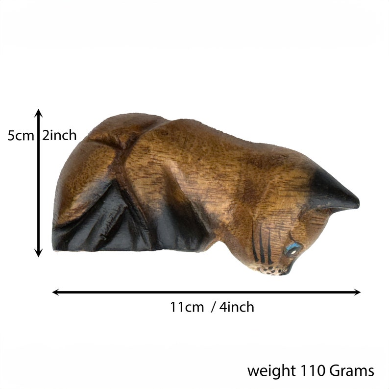 May include: Hand-carved wooden cat figurine in a crouching position. The cat is brown with black markings and blue eyes. It measures 4 inches long and 2 inches tall. weight 110 Grams