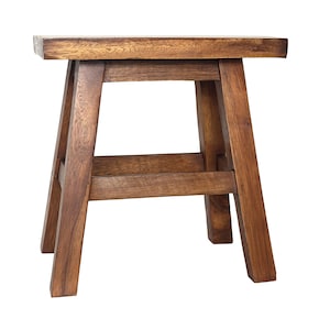 May include: A four-legged wooden stool with a rectangular seat and a dark brown finish. The stool features a sturdy frame with angled legs and a horizontal support brace connecting the legs on each side, showcasing a visible natural wood grain.