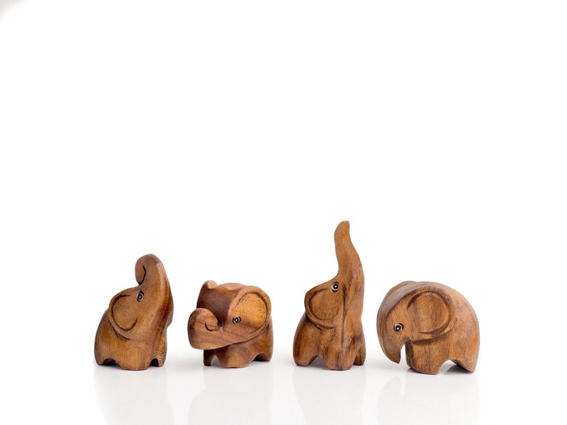 May include: Four wooden elephant figurines in various poses, carved from light brown wood with dark brown accents. The elephants are arranged in a row on a white background.