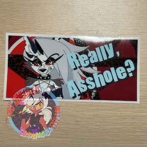 May include: A rectangular sticker featuring a cartoon wolf with the text "Really, Asshole?" in a stylized font. The background has red and black geometric shapes. A smaller, circular sticker with a cartoon character is also visible.