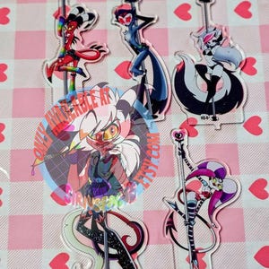 May include: A collection of acrylic character figures, each depicting a unique cartoon figure in various poses. The figures are colorful, with a variety of designs and styles. The background is a pink and white checkered pattern with heart shapes.