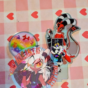 Puede incluir: Una colección de colgantes acrílicos transparentes con personajes de dibujos animados. Un colgante tiene el texto "ONLY AVAILABLE AT SIRIUSFACTS ETSY SHOP". Otro colgante muestra un diseño de arcoíris con animales de globos. El fondo es un patrón de cuadros rosas y blancos con corazones rojos.