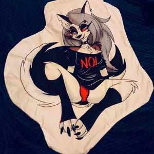 以下が含まれることがあります： 白のグラフィックTシャツ。グレーと黒の毛皮、赤い目、黒のチョーカーをした、狼のような漫画のキャラクターが描かれています。キャラクターは、赤で「NO！」という文字が入った黒いシャツを着ています。デザインは黒で縁取られています。