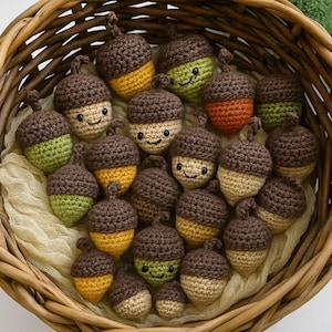May include: A collection of small, crocheted acorn-shaped toys with dark brown caps and bodies in various shades of yellow, orange, and green. Many of the acorns feature embroidered black eyes and a small smile, all arranged inside a woven basket.