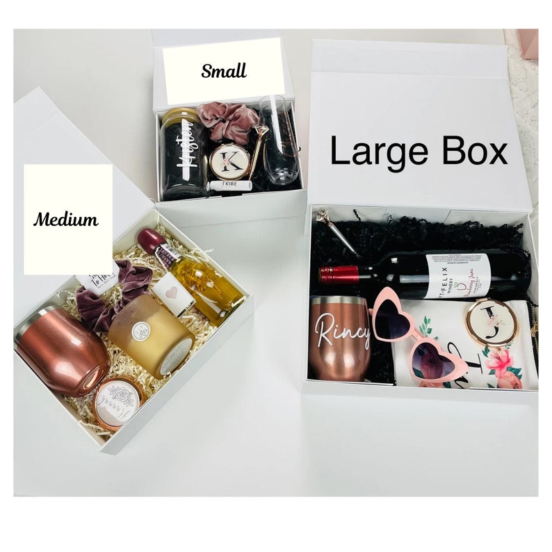 May include: Three gift boxes in different sizes, labeled "Small", "Medium", and "Large Box". Each box is filled with various gifts, including a bottle of wine, a candle, a tumbler, and sunglasses.