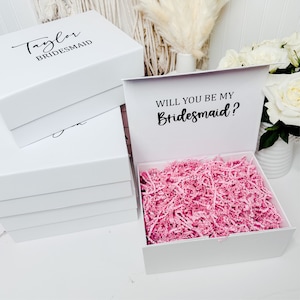 May include: White gift box with a pink tissue paper filler. The lid of the box has the text "Will you be my Bridesmaid?" printed in black.